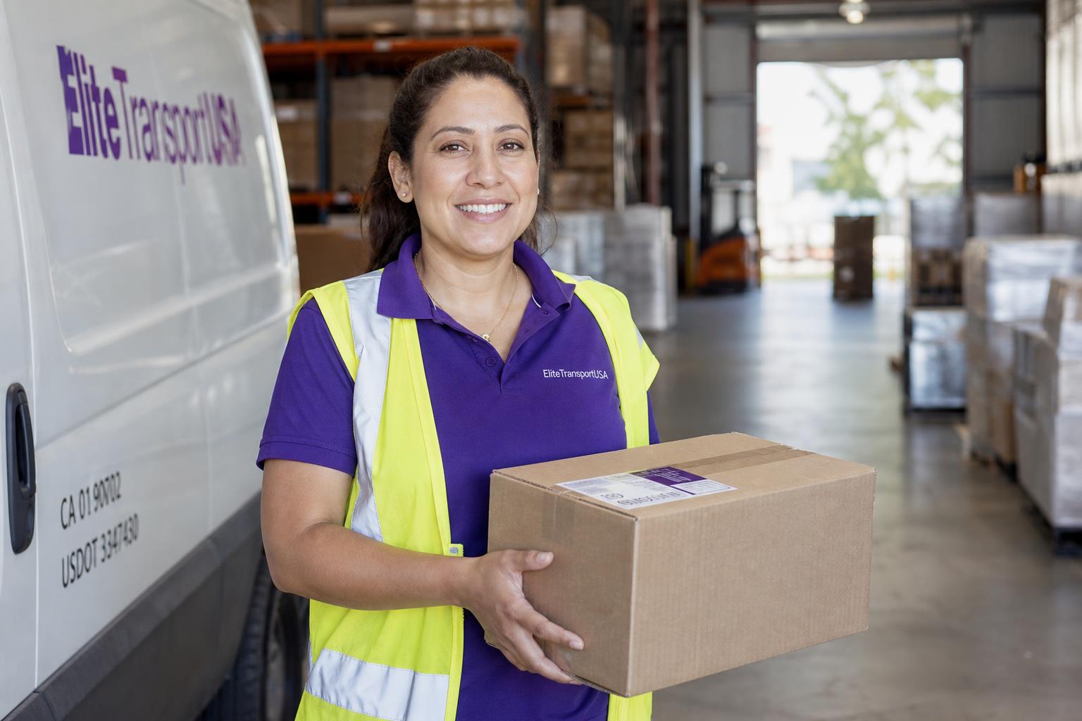 EliteTransportUSA logistics specialist holding a parcel beside a delivery van inside the warehouse